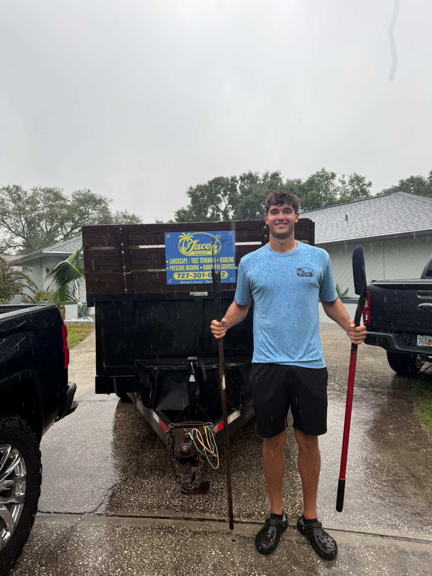 Jace Maples, founder of JaceTM LLC, holding a rake and shovel in front of his work trailer